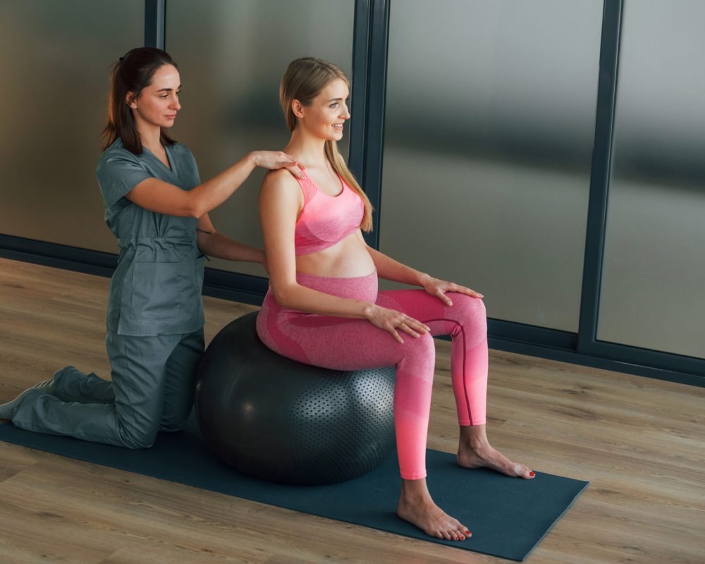 Pregnant woman in pink clothes. In health center getting help by doctor.